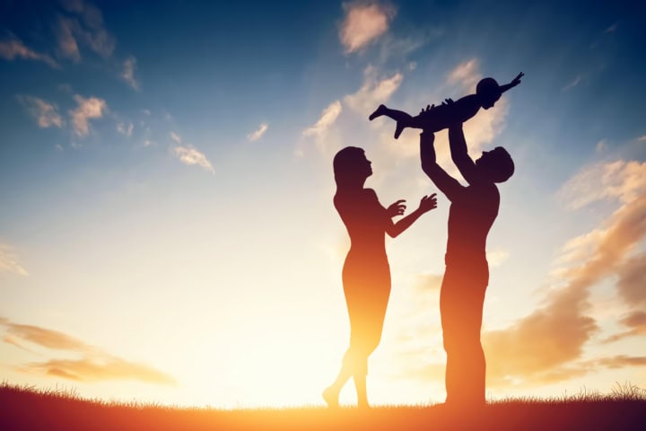 Couple holding a child up to the sky during sunset